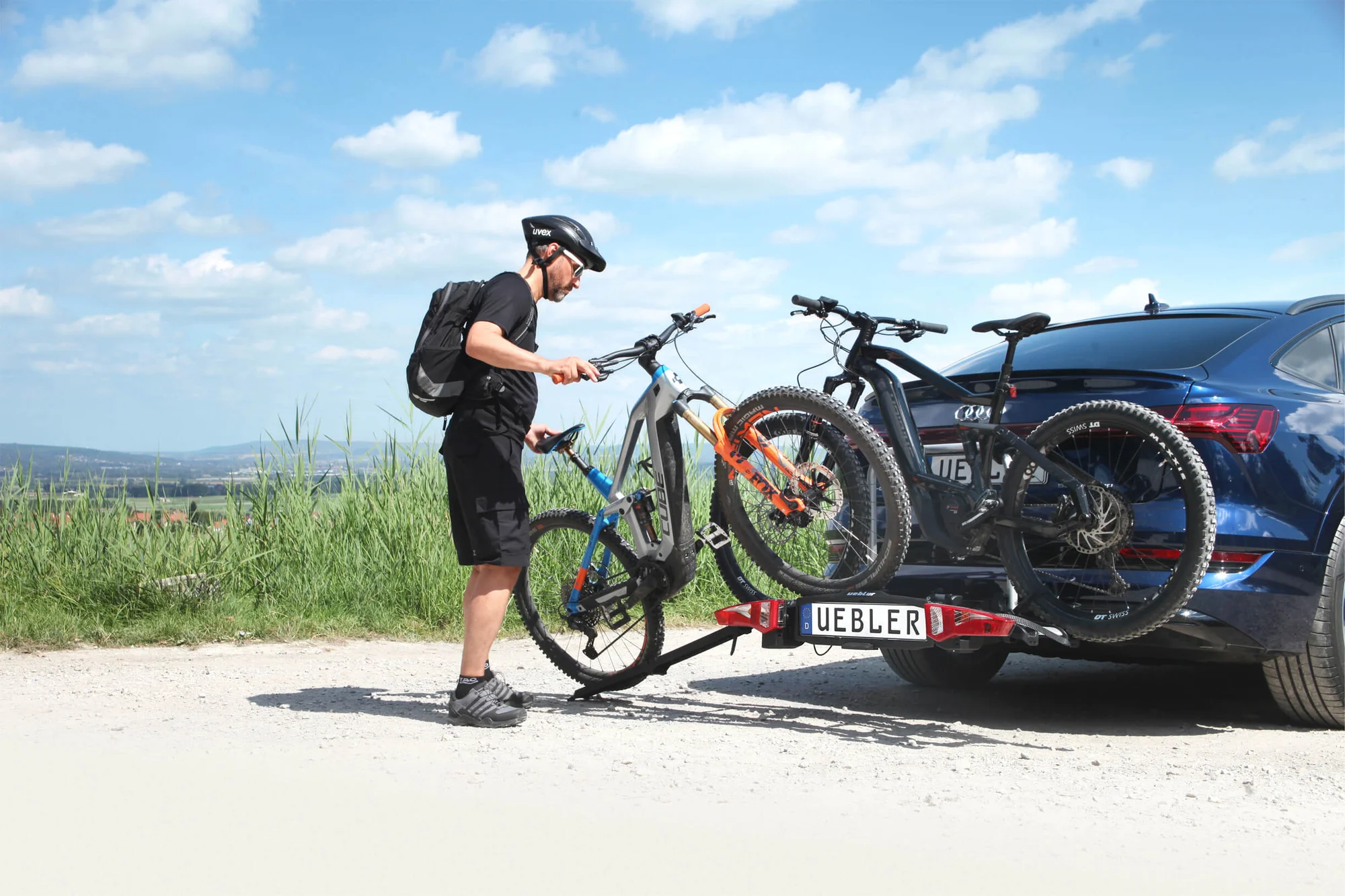 Fietser laadt e-bikes op een Uebler-drager onder een zomerse lucht